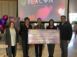 Four people hold a large check in US dollars in front of an a/v/ screen with the Beacon Impatiens logo.